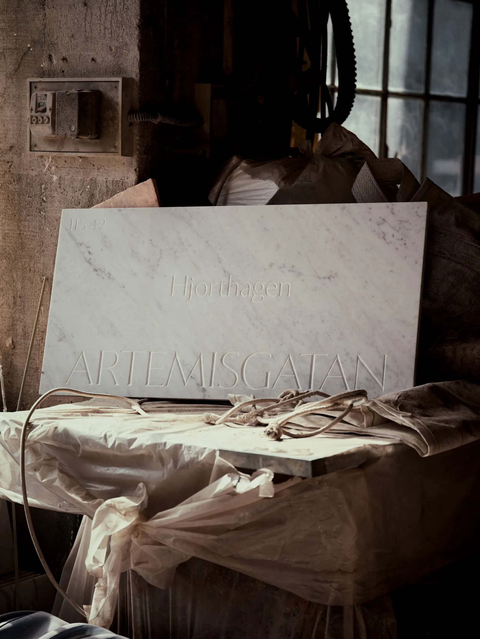The Artemisgatan sign propped inside a marble workshop, surrounded by protective wrapping, rope, and tools.