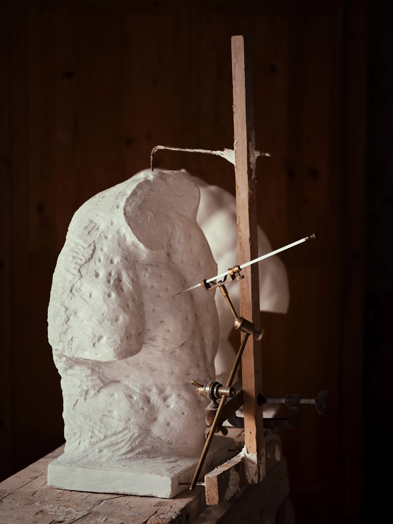 A carved stone torso on a workbench fitted with a pointing machine, the caliper-like tool sculptors use to transfer proportions from a model.