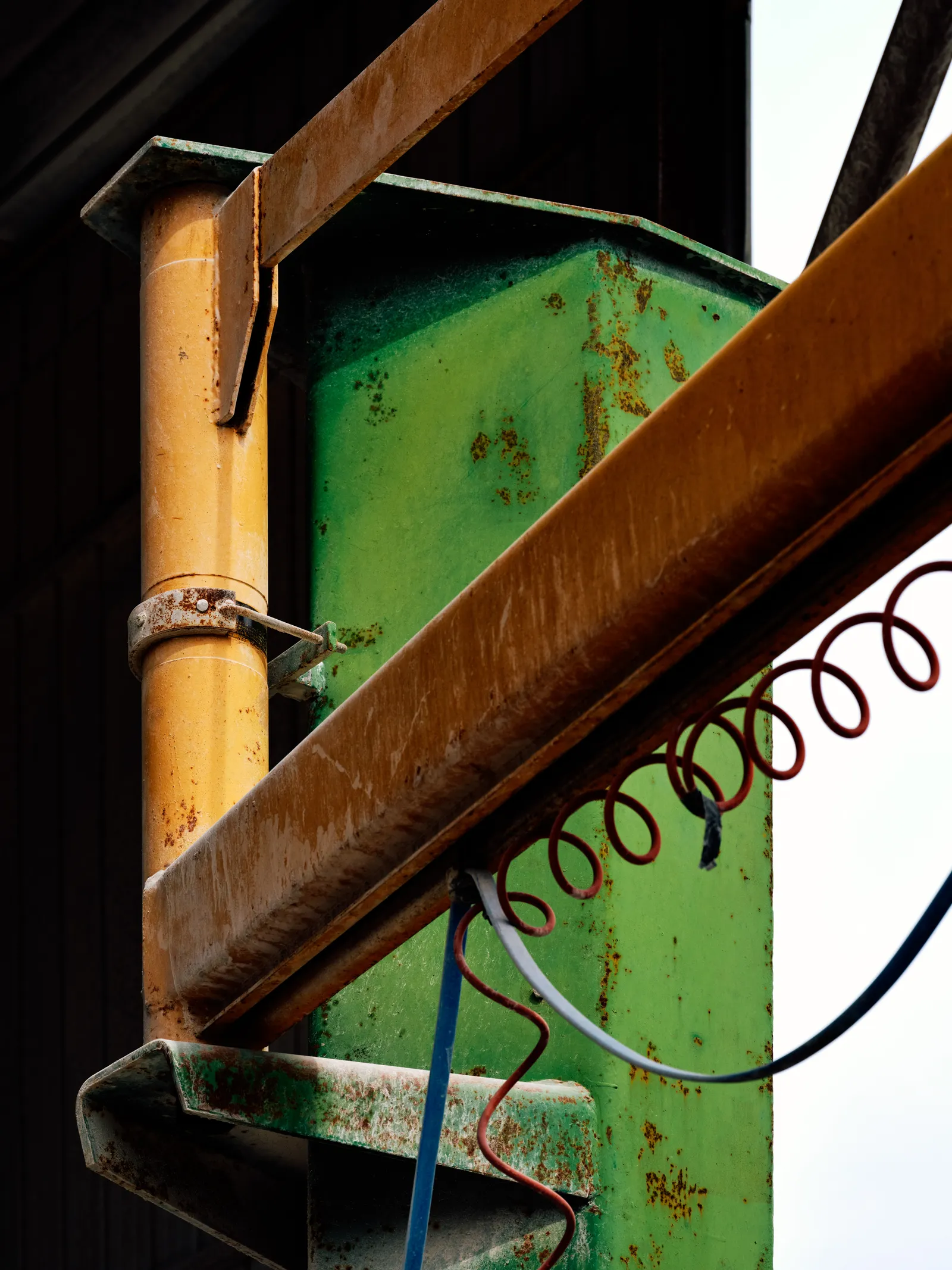 Close-up of weathered steel crane beams and coiled hoses against a rusted green pillar.
