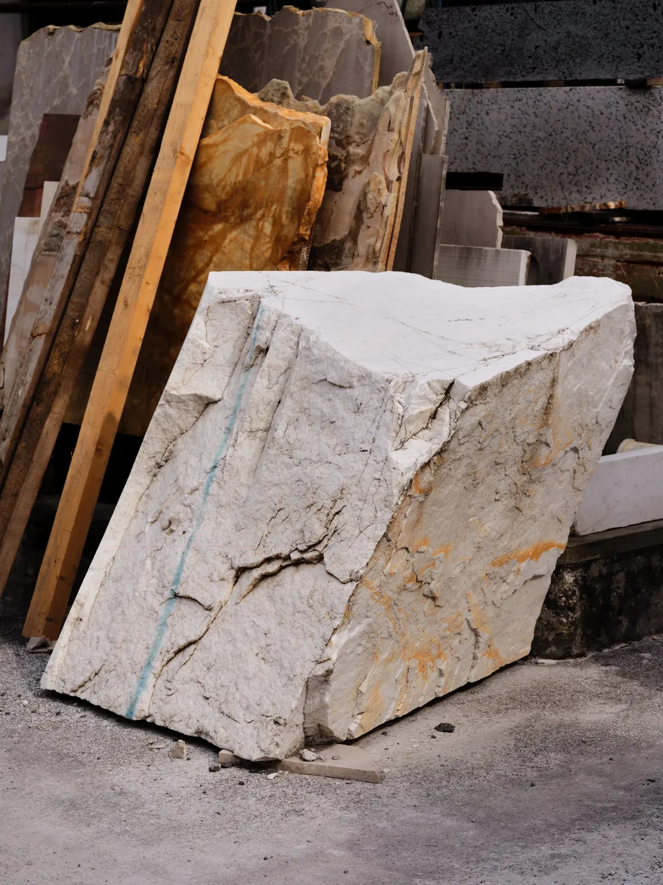 A roughly hewn block of white marble with golden veining, standing in a stone yard.