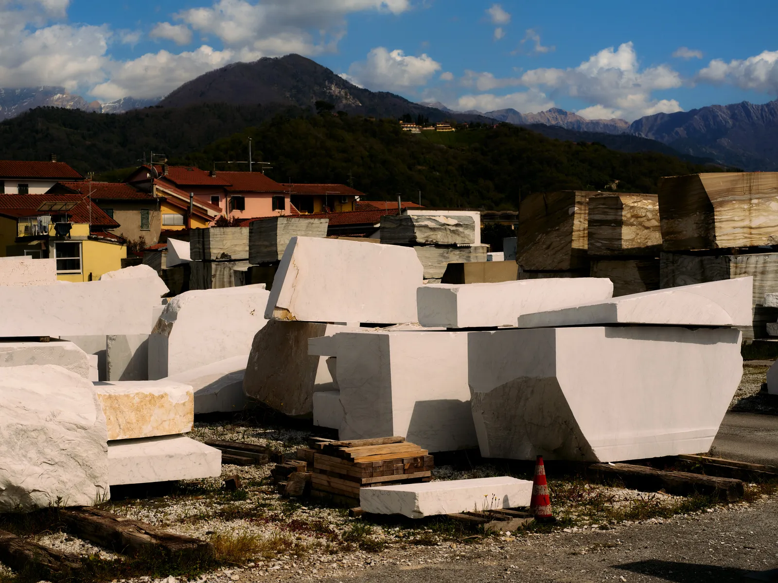 A Carrara marble yard filled with rough-cut blocks, colorful houses and the Apuan Alps rising behind.