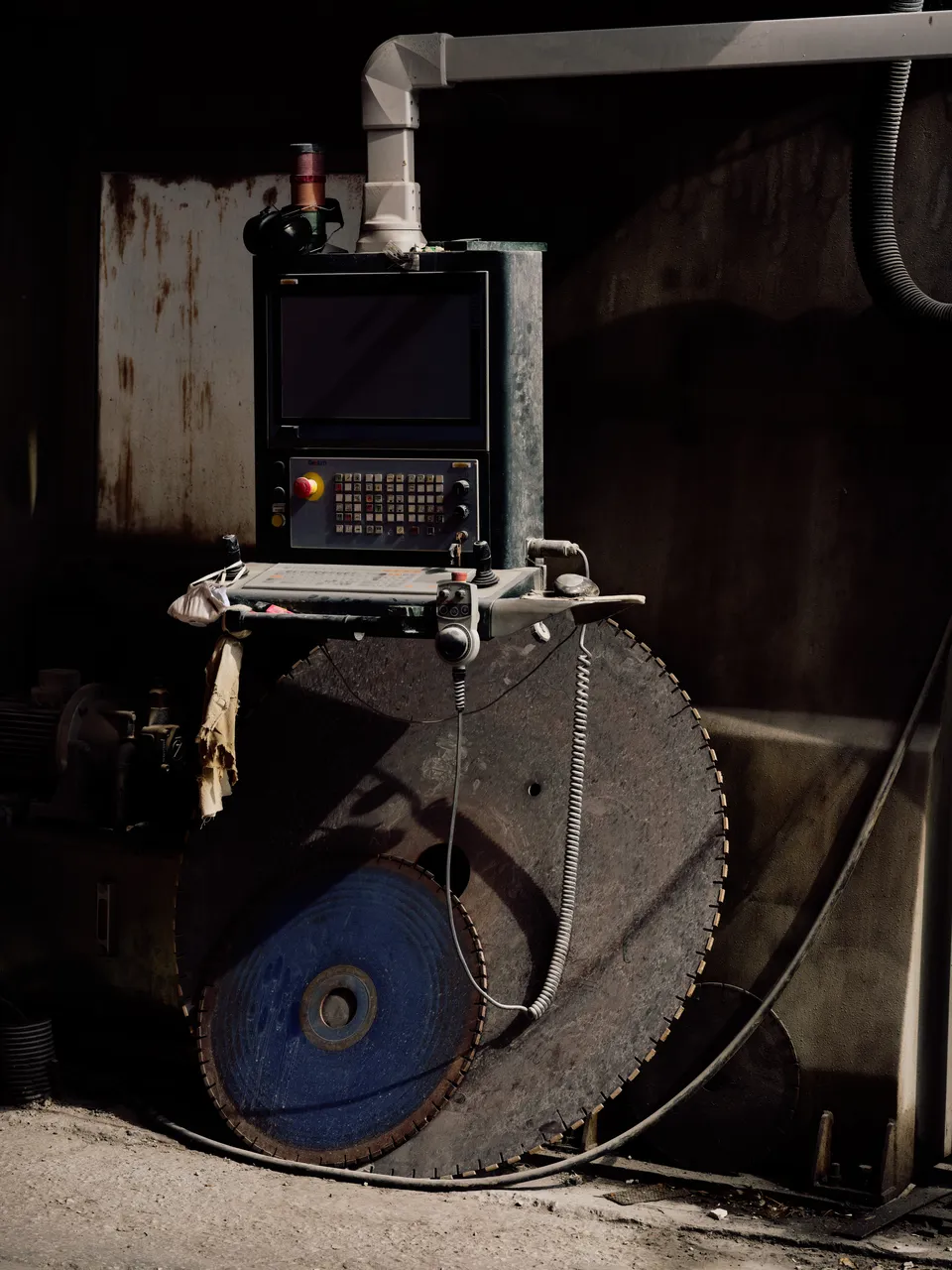 A large circular stone saw with a CNC control panel, in a dim workshop.