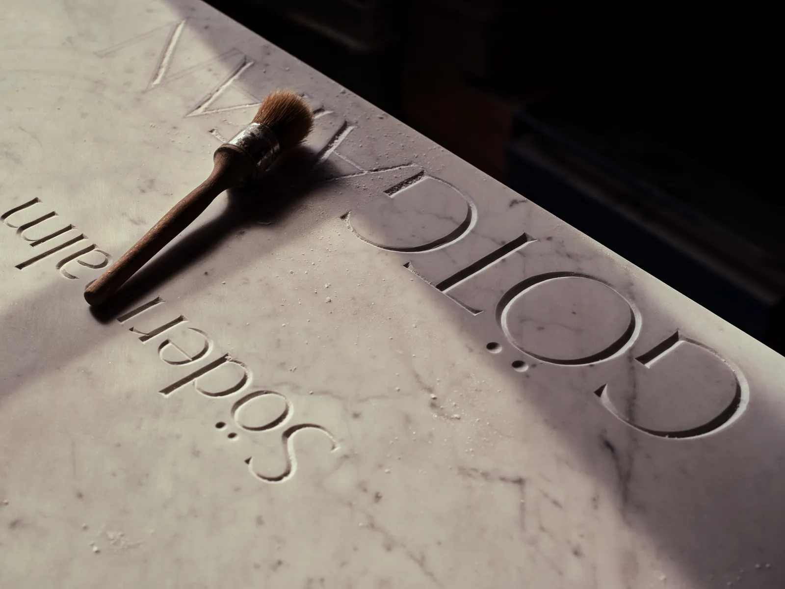 A carver’s dusting brush resting on freshly carved lettering, clearing marble dust from the cut.