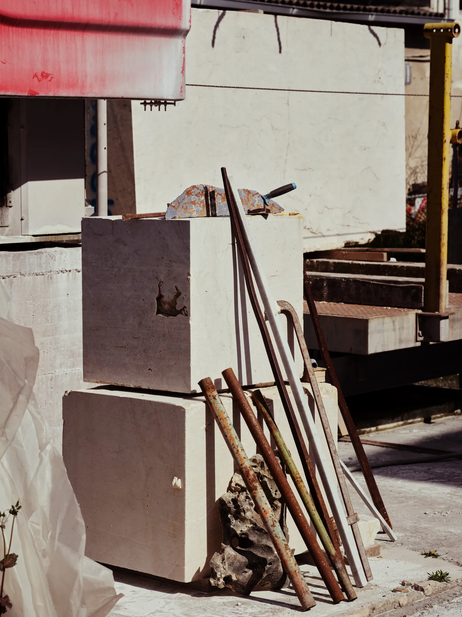 Pale stone blocks and hand tools leaning together outdoors under a striped awning in a stone yard.