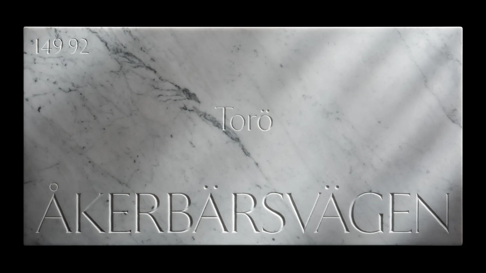 The Åkerbärsvägen marble sign photographed straight-on against black, its street name and postal code cut into the stone.