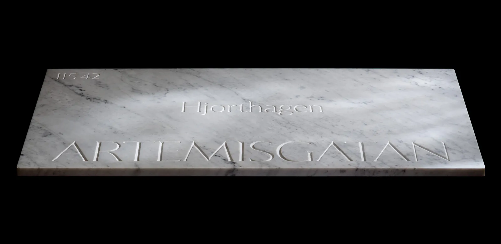 The Artemisgatan marble sign photographed at an angle against black, light catching its carved surface.