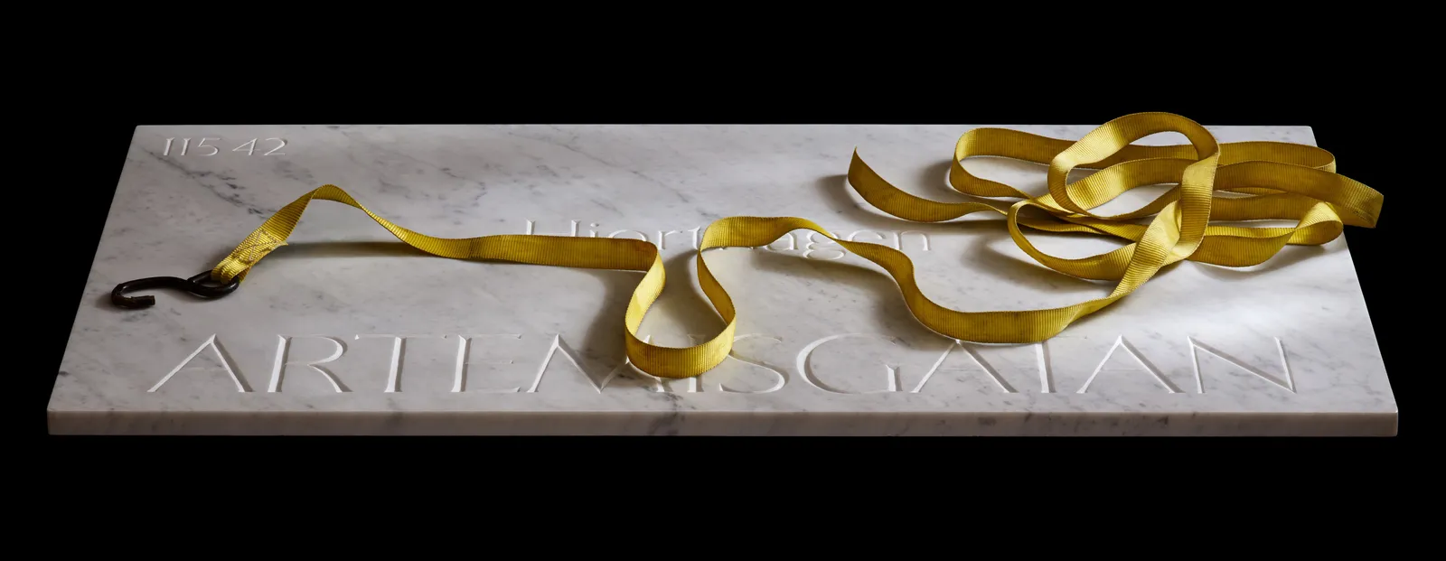 The Artemisgatan marble sign on black, a coiled yellow tie-down strap resting across it mid-transport.