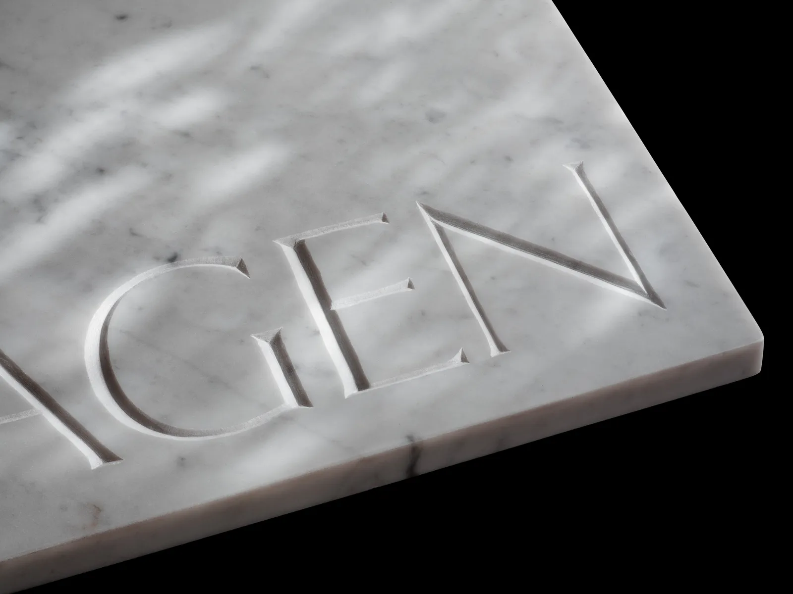 Extreme close-up of carved marble letters in raking light, showing the V-shaped cut of the incision.