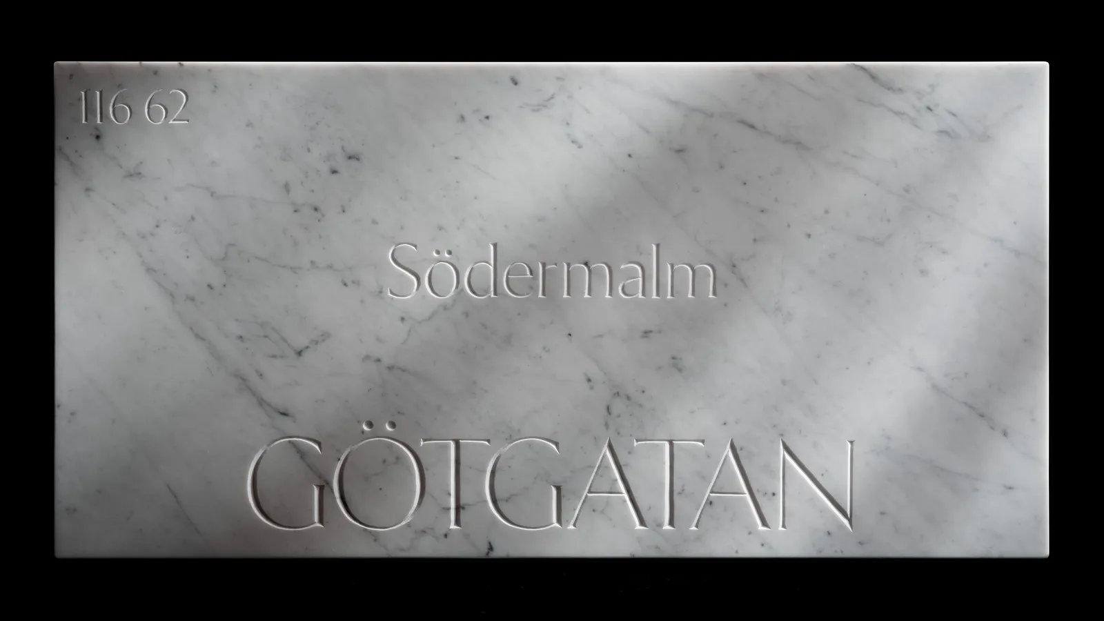 The Götgatan marble sign photographed straight-on against black, its street name and postal code cut into the stone.